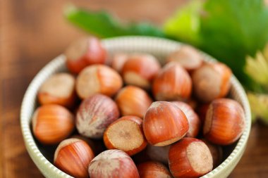 Ahşap bir masada yeşil yaprakları olan yuvarlak yeşil bir kasede fındıklar. Tarım organik, olgun fındık. Fındık bolluğu. Organik biyolojik fındık. Sağlıklı şişmanlar. Yeşil yapraklı fındıklar.. 