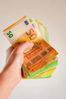 Beyaz arka planda bir elde para. Avro banknotları sayılıyor. Avrupa ülkelerindeki giderler ve gelirler. Yakın planda bir paket para..