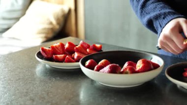 Mutfakta çilekleri ikiye bölmek. Yavaş çekim. Kahvaltı hazırlama süreci. Eller taze çilek keser ve tabağa koyar. Servis için çilek hazırlıyorum. 4k görüntü