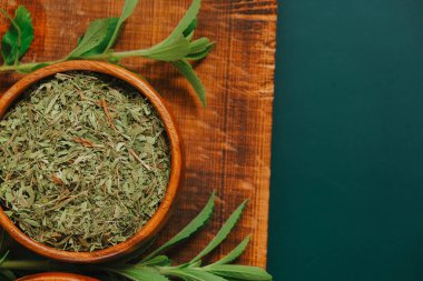 Stevia rebaudiana yuvarlak ahşap kasede kuru toz ve koyu yeşil arka planda tahta üzerinde taze bitki dalları. Tatlı yaprak şekeri yerine. Diyet gıda tatlandırıcı. Tatlı bitki..
