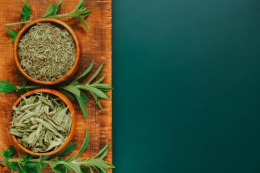 Stevia kuru yapraklar ve yuvarlak ahşap kaselerde pudra ve koyu yeşil bir zemin üzerinde tahta dallar. Tatlı yaprak şekeri yerine. Beslenme yiyeceği tatlandırıcı. Tatlı bitki..