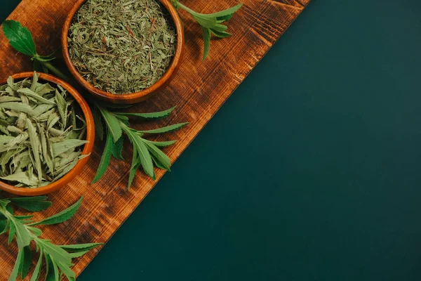 Stevia dry leaves and powder in bowls and fresh plant branches on a wooden board on a dark green background.sweet leaf sugar substitute.Dietary food sweetener.sweet plant.