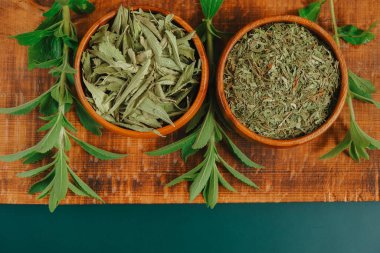 Tatlı bitki. Stevia kuru yapraklar ve yuvarlak ahşap kaselerde toz ve koyu yeşil arka planda tahta üzerinde taze bitki dalları. Tatlı yaprak şekeri yerine. Beslenme yiyeceği tatlandırıcı..