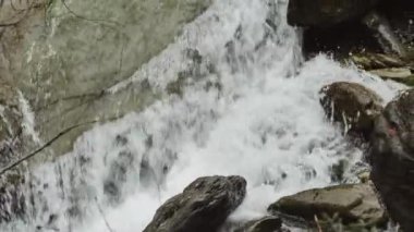 Fırtınalı dağ nehri. Su, büyük kaya ve taşların üzerine kaynar ve dökülür. Bir dağ nehrinin damlaları ve sıçramalarıyla dolu fırtınalı su akıntısı. Ağır çekim. Su ve taş dokusu. 4k görüntü