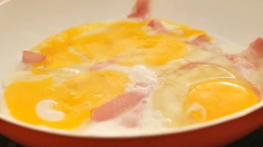 Yumurtalı kızarmış domuz yağı. Fırının üstünde turuncu bir tavada jambonlu sahanda yumurta. Çırpılmış yumurta. 4k görüntü