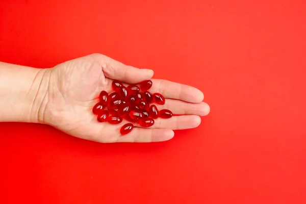 stock image Krill oil capsules in a womans hand on a red background .Healthy eating and food supplements. Dietary supplements and food supplements