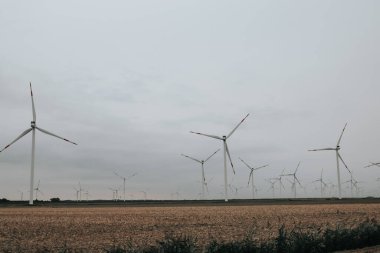 Rüzgâr değirmenleri sisli ve bulutlu bir havada bir tarlaya kurulur. Yeşil Enerji Kaynağı. Doğal yenilenebilir temiz eko enerji. Çevre dostu doğal enerji kaynağı.. 