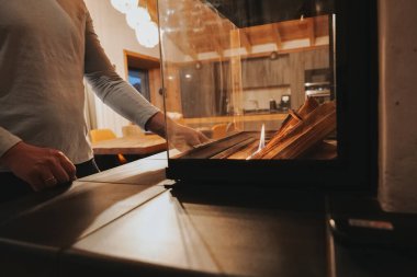 İçerideki cam şömine. Elleri çakmaktaşı tutuyor ve yakacak odun yakıyor. İçeride şömine var. Şömineyi yak. Sıcak sıcak ev atmosferi