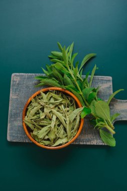 Stevia rebaudiana. Tatlı bitki. Stevia, kablardaki kuru yapraklar ve koyu yeşil arka plandaki taze bitki dalları. Tatlı yaprak şekeri yerine..