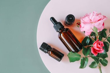 Gül suyu. Gül özlü organik kozmetik. Gri arka planda pembe bir kürsüde cam bir şişede gül yağı. Aromaterapi ve kozmetik. Organik doğal gül yağı. Organik biyokozmetik.