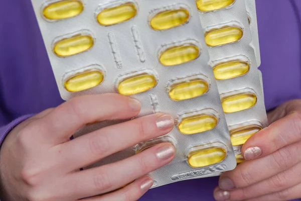 Omega fatty acids in jelly capsules.Fish oil capsules in blisters in hands in a purple sweatshirt.Healthy fats and womens health.Dietary supplements and vitamins in womens nutrition.
