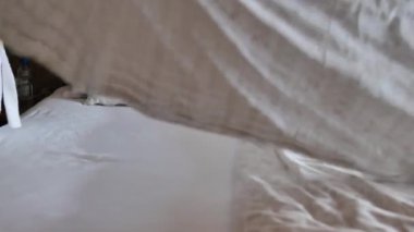 Yatak hazırlıyorum. Beyaz bornozlu bir kadın yatağı topluyor. Yatak odasında sabah temizliği rutini. Kadınların elleri yatağın üzerindeki battaniyeyi düzeltiyor. 4k görüntü