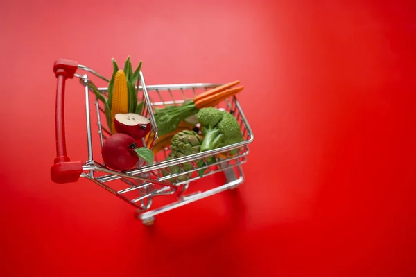 Shopping cart with groceries on a red background.grocery consumer basket.food cost.Vegetables and fruits price increase.food crisis.Decorative supermarket trolley with groceries on a red background.