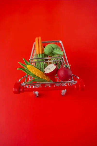 grocery consumer basket.food cost.Vegetables and fruits price increase . supermarket trolley with groceries on a red background. food crisis.Decorative vegetables and fruits.