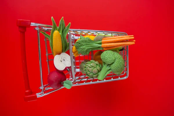 Shopping cart with groceries on a red background.grocery consumer basket.food cost.Vegetables and fruits price .food crisis.Decorative supermarket trolley with groceries on a red background.