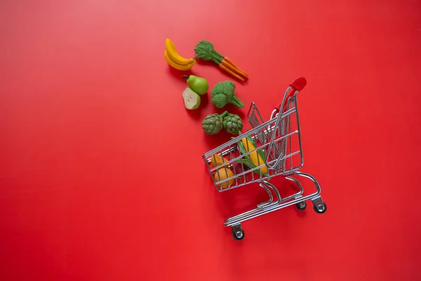 grocery consumer basket.food cost.Rising food prices.Shopping cart with groceries on a red background.Vegetables and fruits price increase.food crisis.Decorative vegetables and fruits.Decorative