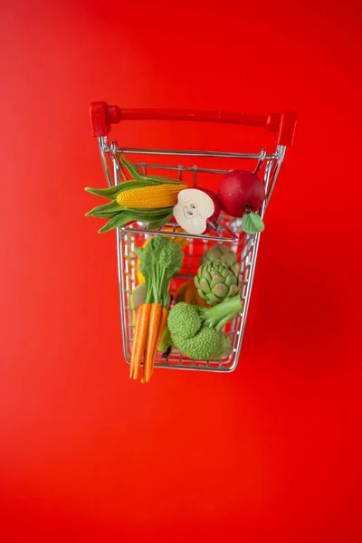 grocery consumer basket on a red background.food cost.Vegetables and fruits price increase.food crisis.Decorative supermarket trolley with groceries on a red background.