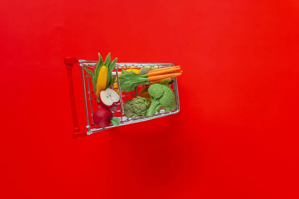 food cost. Shopping cart with groceries on a red background.grocery consumer basket.Vegetables and fruits price increase.food crisis.Decorative supermarket trolley with groceries on a red background.