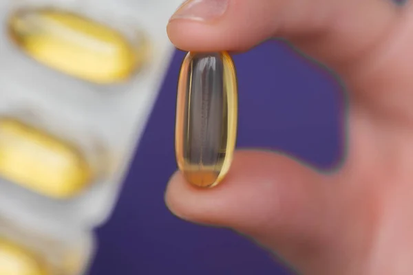 Fish oil for womens. Fish oil capsules in female hands in a purple sweatshirt.Omega fatty acids jelly capsules.Healthy fats and womens health.Dietary supplements and vitamins in womens nutrition.