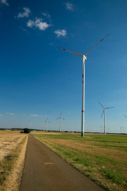 Yel değirmenleri mavi gökyüzü arka planında yol boyunca ilerledi. Rüzgar jeneratörleri manzarası. Doğal yenilenebilir temiz eko enerji. Alternatif enerji kaynakları. Çevre dostu doğal enerji kaynağı.. 