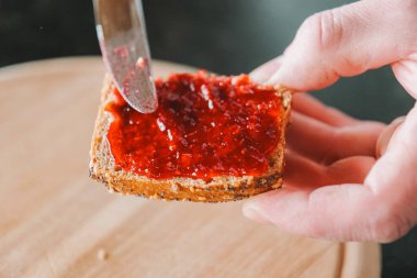 Reçelli tost. Ahududu reçelli çörek. Tatlı kahvaltı. Eller ahududu reçelini tam tahıllı çöreğe yayar..