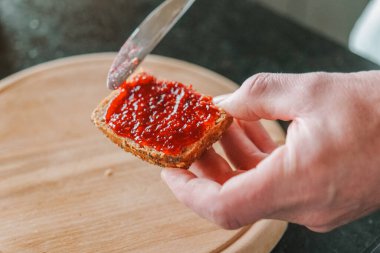  Kahvaltı yemeği. Ahududu reçelli çörek. Tatlı kahvaltı. Eller bütün bir tahıllı çöreğe ahududu reçeli sürer. Kahvaltıyı hazırlıyorum. Ahududu reçelli tam tahıllı çörek..