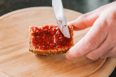 Ahududu reçelli çörek. Eller bütün bir tahıllı çöreğe ahududu reçeli sürer. Kahvaltıyı hazırlıyorum. Ahududu reçelli tam tahıllı çörek. Geleneksel kahvaltı yemeği.