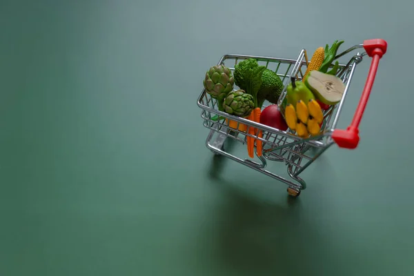 food basket cost.Rising food prices.Shopping cart with groceries on green background.Vegetables and fruits price.Decorative supermarket trolley with groceries.Food prices.