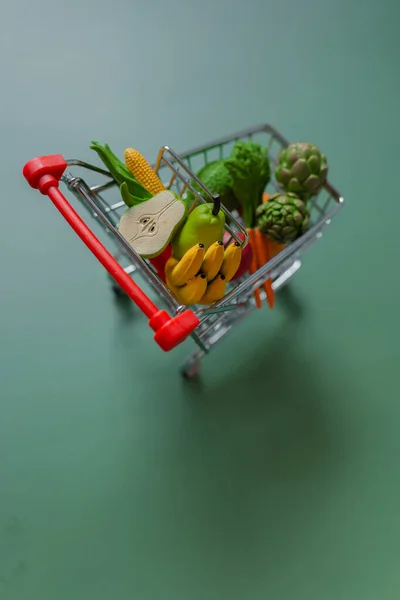 Food basket cost.Rising food prices.Shopping cart with groceries on green background.Vegetables and fruits price.Decorative supermarket trolley with groceries.Food prices.