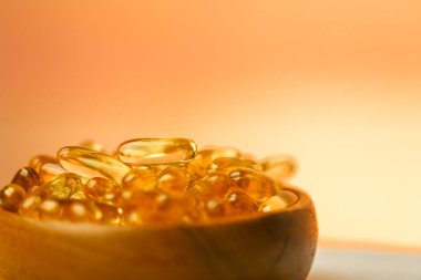 Bulanık turuncu arka planda ahşap bir kaptaki balık yağı kapsülleri. Jöle kapsüllerinde Omega yağ asitleri. Beslenme takviyeleri ve vitaminler..