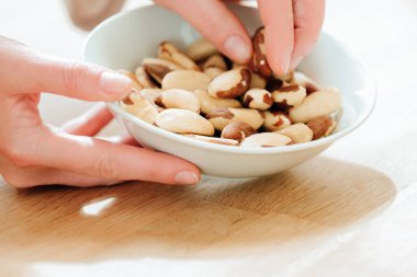 Fındık ve tohum. Brezilya fındığı elinde beyaz bir seramik bardakta ahşap bir masada. Diyetteki sağlıklı yağlar. El, Brezilya fındıklarını yakın plandan alıyor. Faydalı, sağlıklı bir atıştırmalık. Brezilya fıstığı diyette.