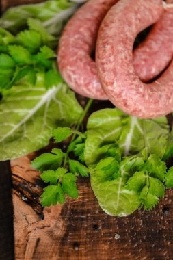 Köy usulü sosisler. Çiğ sosis halkaları, taze maydanoz, ahşap bir tahtanın üzerinde marul yaprakları..