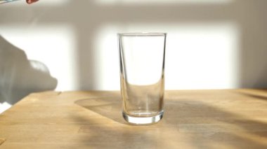 Temiz su bardağı. Su, şeffaf bir bardağa dökülüyor. Parlak bir mutfakta, ahşap bir masada. Su jeti ağır çekimde. İçme modu. 4k görüntü
