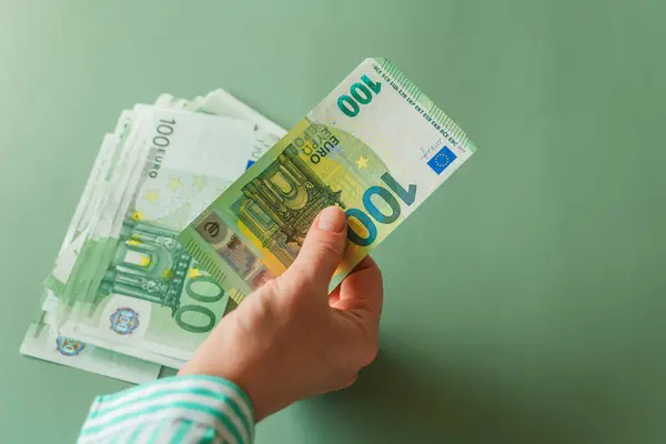 Income of women in European countries.salary of a woman in the Eurozone.Hands in a green shirt holding euro money on a green background