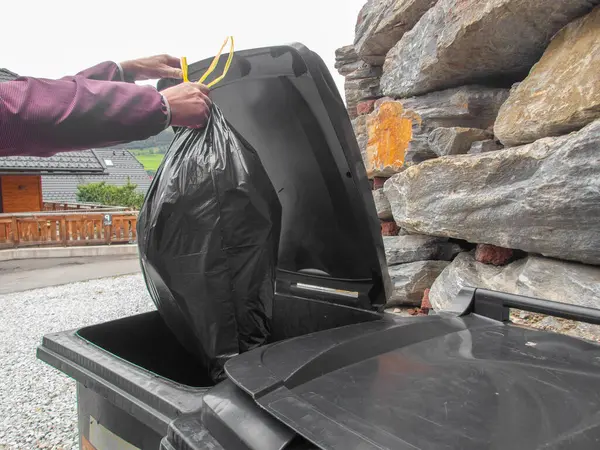 Garbage plastic bag.Sorted garbage. hand lowers a black bag of garbage into a plastic trash bin.Separate waste sorting.
