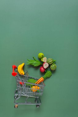 Yiyecek alışverişi geçmişi. Yeşil zemin üzerinde dekoratif sebzeler ve meyvelerle süpermarket arabası. Artan gıda fiyatları. Sebze ve meyve fiyatları.