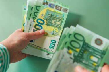 Avro Bölgesi 'ndeki bir kadının yeşil zemin üzerinde çalışan 100 avroluk banknotlar. Avrupa ülkelerindeki kadın gelirleri. Avro paralarını tutan eller. Avro Bölgesi 'nde kazançlar ve harcamalar.