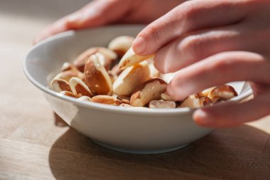 Brezilya fındığı, güneşteki ahşap bir masada el ele fındık ezmesi. El, Brezilya fındıklarını tabaktan alır. Sağlıklı şişkolar. Faydalı sağlıklı atıştırmalık.