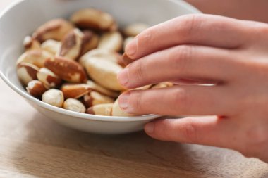 Brezilya fındığı beyaz bir fincanda. El tabaktan Brezilya fındığı alır. Sağlıklı şişkolar. Keto diyet malzemesi. Faydalı sağlıklı atıştırmalık..
