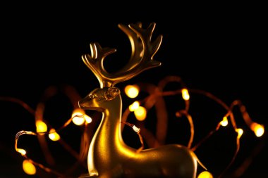 Noel arkaplanı. Siyah bir arka planda altın geyik ve altın çelenk. Parlak dekoratif bir nesne. Karanlık bir arka planda Noel geyiği ve çelenk. 