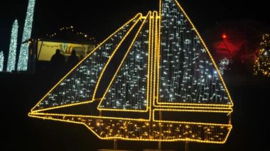 Karanlıkta parlayan çelenklerden yapılmış pırıl pırıl bir gemi. Noel süsleri. Parlak dekoratif tatil eşyaları. 4k görüntü