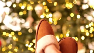Noel sıcacık havası. Çiçek arka planında bir Noel ağacında kürk terlik giymiş bacaklar. Kış tatili ve dinlenme. Yüksek kalite 4k görüntü