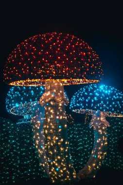 Çok renkli çelenklerden Noel mantarları. Karanlıktaki çelenklerden parlayan Noel figürleri. Çelenklerle kurulmuş..