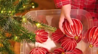 Noel ağacı topları. Ekose pijamalı çocuk kırmızı Noel toplarını kutudan alıyor. 4k görüntü