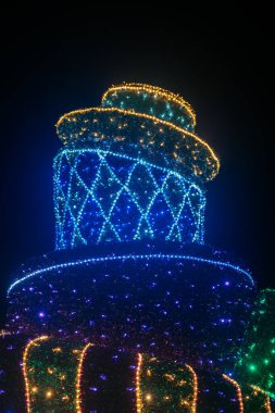 Noel sokak dekorasyonu. Karanlıkta parlayan pasta objesi. Karanlıkta yeşil, mavi ve mor çelenklerden yapılmış pasta.