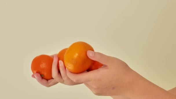 タンジェリン柑橘類のフルーツ ベージュの背景に子供の手のタンジェリン 赤ちゃんの食べ物のためのビタミンC 有機果物の自然な源 4K映像について — ストック動画