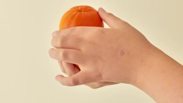柑橘類のフルーツ ベージュの背景に子供の手のタンジェリン 赤ちゃんの食べ物のためのビタミンC 有機果物の自然な源 4K映像について — ストック動画