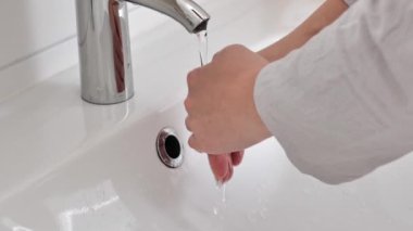 El yıkama işlemi. Beyaz bir lavabonun üzerinde akan suyun altında ellerini yıkıyor. 4k görüntü