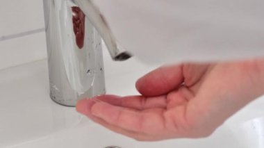 El yıkama işlemi. Beyaz seramik lavabonun üzerinde akan suyun altında ellerini yıkıyor. Ağır çekim. Temizlik ve hijyen kavramı. 4k görüntü