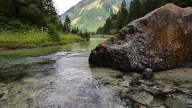 Dağ nehri, bir dağ manzarasının arkasındaki kayanın yanında akar. Güzel bir dağ manzarası. Alp dağı rezervleri. Ağır çekim. 4k görüntü